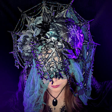 Person wearing an elaborate headpiece with spiderweb design, crab and purple accents on a dark background