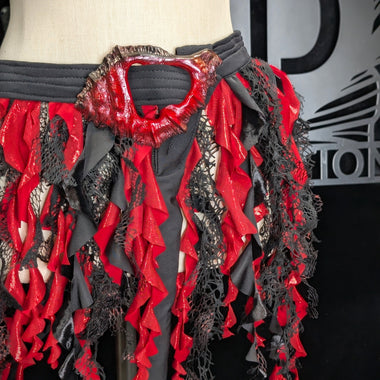 Mannequin wearing a red and black ruffled garment with a brand logo in the background.