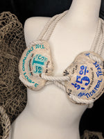 Mannequin wearing a bra made of rope with text on it, against a dark background.
