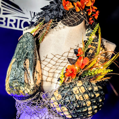 Mannequin with Alligator decorative top and headpiece featuring flowers and netting, with a blurred background.