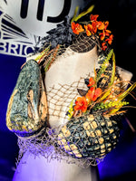 Mannequin with Alligator decorative top and headpiece featuring flowers and netting, with a blurred background.