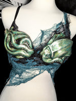 Mannequin wearing a bra with green alien-like squid designs on a black background