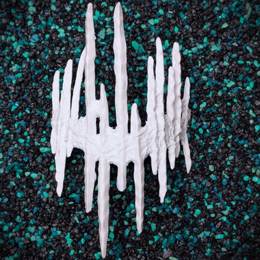 A white textured, spiky decorative base for a blind mask crown resembling icicles or a stylized crown, photographed from above on a black and teal pebble surface.
