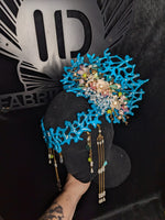 Blue fan coral and floral headpiece with beads held by a hand against a dark background