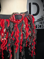 Mannequin wearing a red and black ruffled garment with a brand logo in the background.