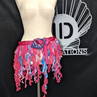 Colorful fringe skirt on a mannequin with a black background and logo.