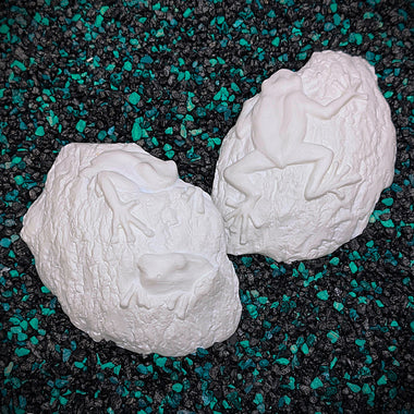 Two white ceramic mermaid figures on a black and green speckled surface