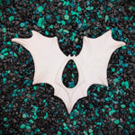 White bat-shaped earrings on a textured black and green background