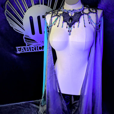 Mannequin wearing a decorative costume with a cape in front of a dark background with 'Fabric' branding.