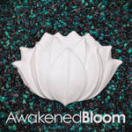 A white resin plastic lotus-shaped DIY mermaid top component with a textured surface, displayed on a bed of black and teal pebbles. The Style name 'AwakenedBloom' is printed in white text at the bottom.