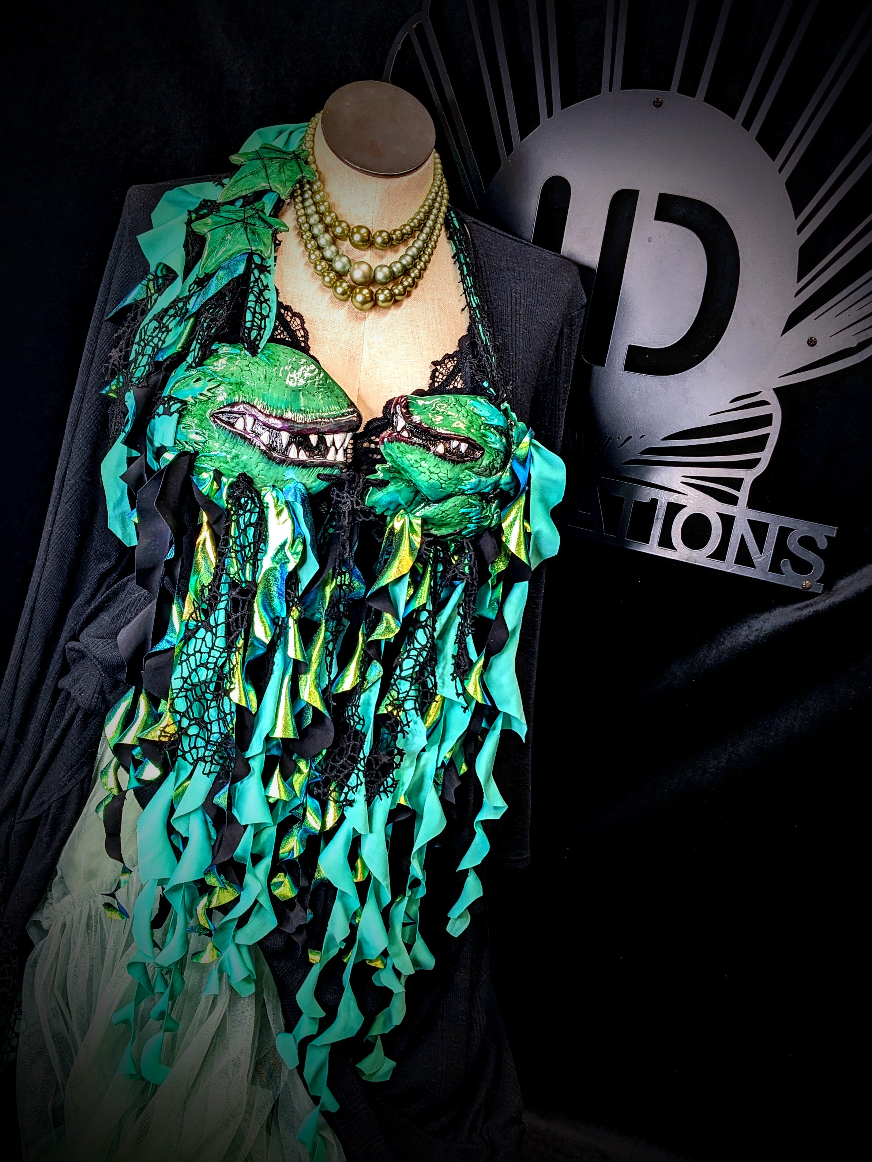 Mannequin wearing a green and black decorative garment with a brand logo in the background