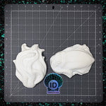 Two white plastic molds of squid shapes on a grid cutting mat with ID Fabrications logo.