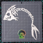 A white hand cast plastic resin fish skeleton model displayed on a gray gridded cutting mat with a visible ID Fabrications logo.